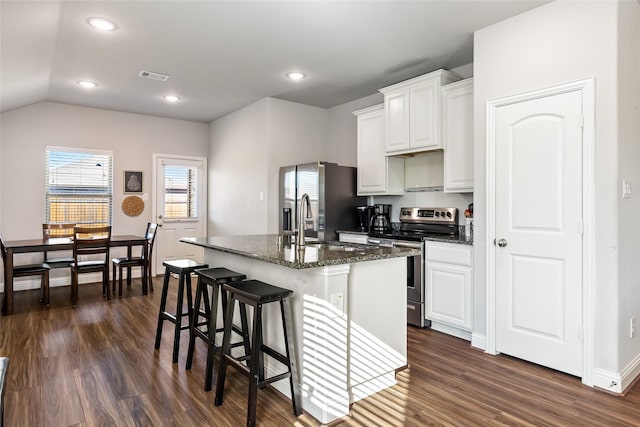 kitchen with dark wood-style floors, stainless steel appliances, visible vents, white cabinets, and an island with sink