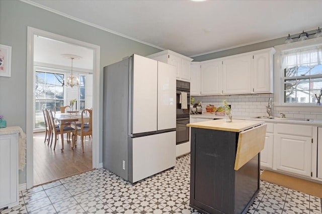 kitchen with a sink, white cabinets, ornamental molding, freestanding refrigerator, and light floors