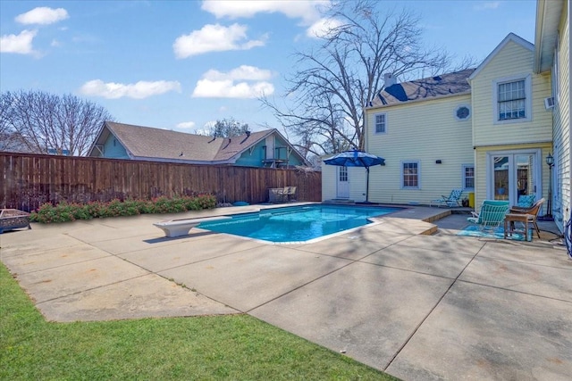 view of swimming pool featuring a fenced backyard, a diving board, a patio, and french doors