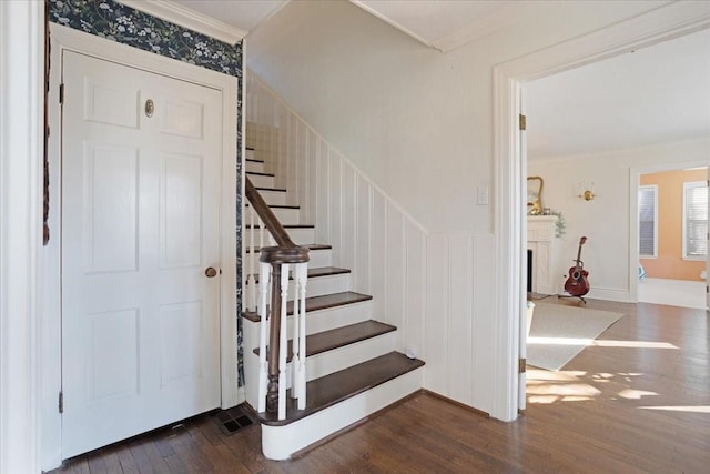 staircase with a fireplace, crown molding, and wood finished floors