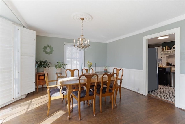 dining room featuring a wainscoted wall, ornamental molding, dark wood-style flooring, and an inviting chandelier