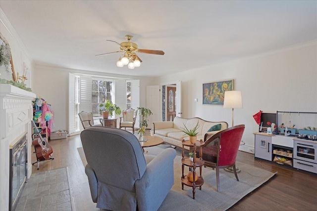 living area with a ceiling fan, a fireplace with flush hearth, ornamental molding, and wood finished floors