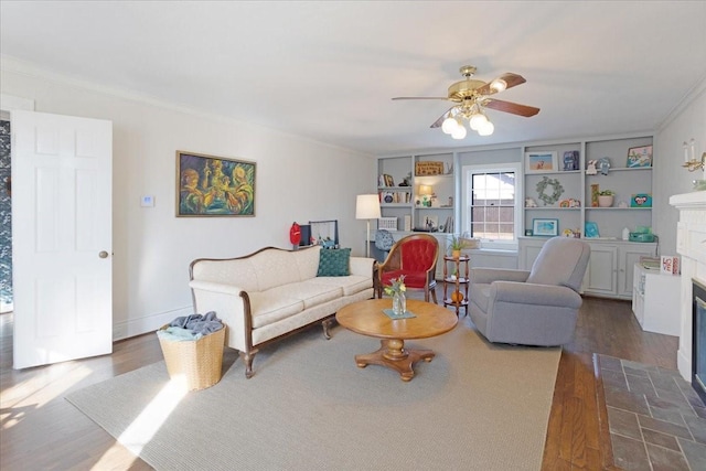 living room with crown molding, dark wood finished floors, a fireplace with flush hearth, a ceiling fan, and baseboards