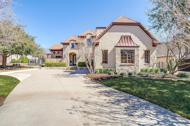 view of front of home with a standing seam roof, driveway, brick siding, and a front lawn