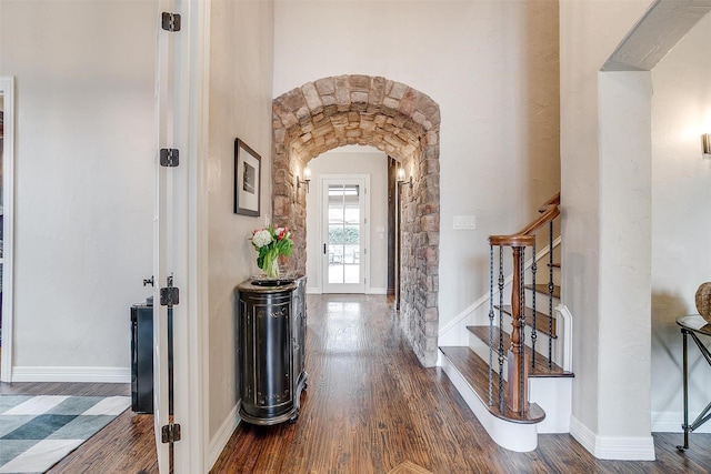 entrance foyer featuring arched walkways, wood finished floors, stairs, and baseboards