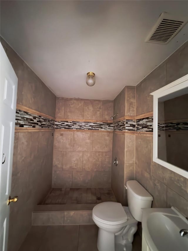 bathroom with visible vents, toilet, a tile shower, a sink, and tile patterned floors