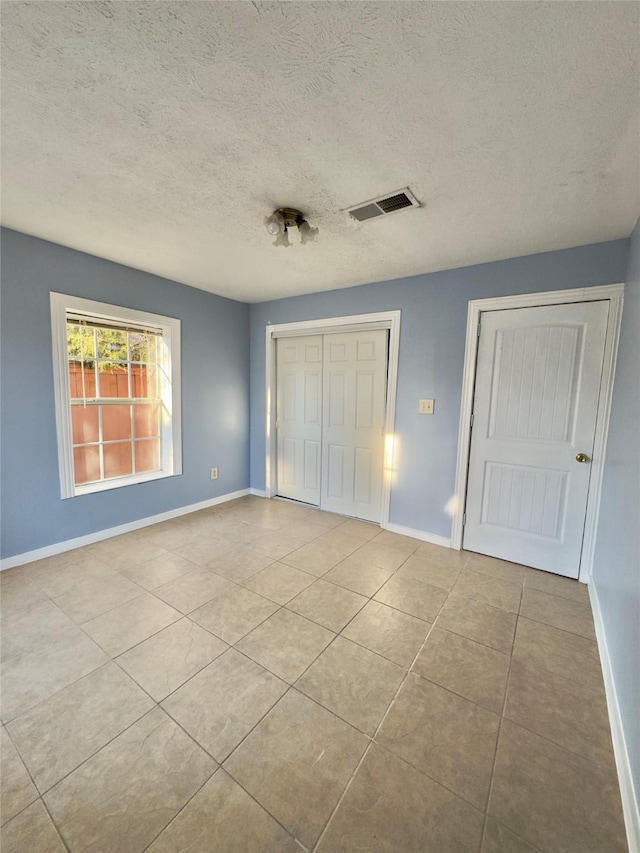 unfurnished bedroom with a closet, visible vents, a textured ceiling, baseboards, and tile patterned floors