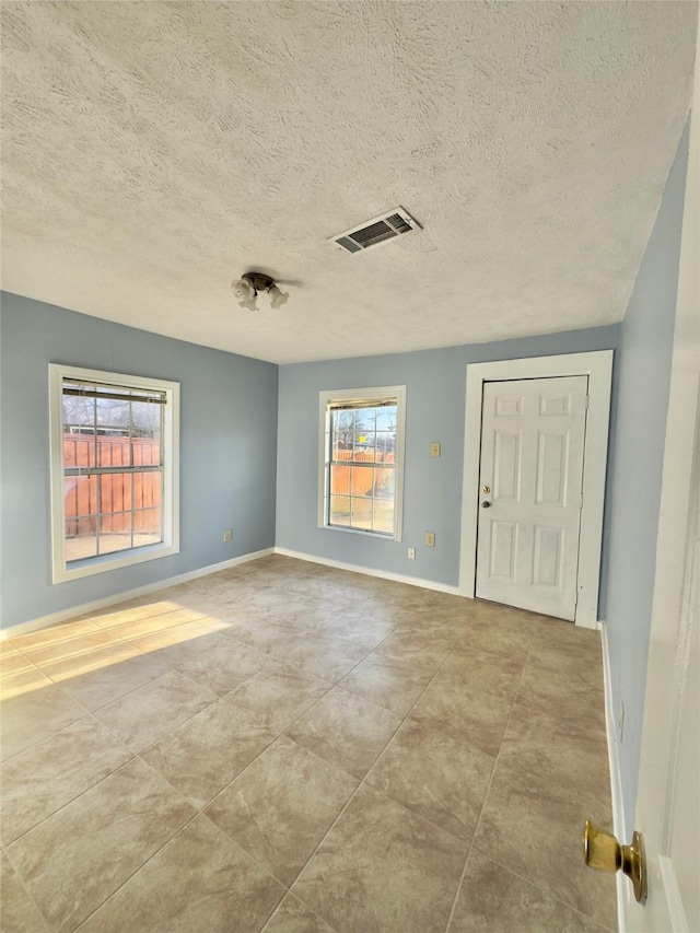 spare room featuring baseboards, visible vents, and a textured ceiling