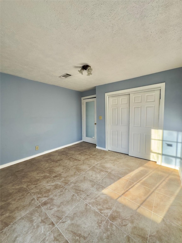 unfurnished bedroom featuring a textured ceiling, tile patterned floors, visible vents, and baseboards