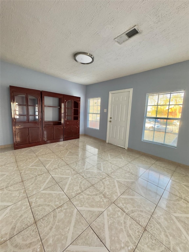 interior space featuring visible vents, a textured ceiling, and baseboards