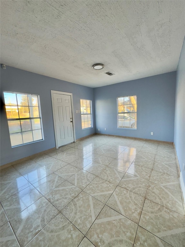 empty room with a textured ceiling, marble finish floor, visible vents, and baseboards