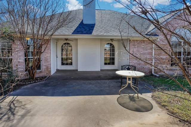 property entrance with a shingled roof, a patio area, brick siding, and a chimney