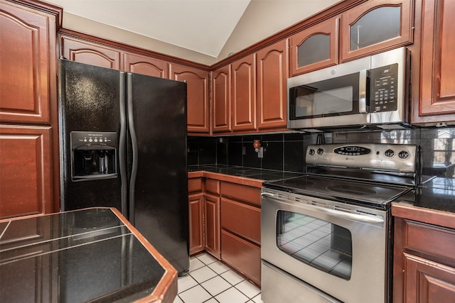 kitchen featuring light tile patterned floors, stainless steel appliances, dark countertops, lofted ceiling, and tasteful backsplash