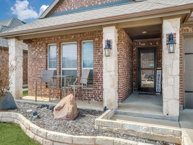 doorway to property featuring a shingled roof, covered porch, and brick siding