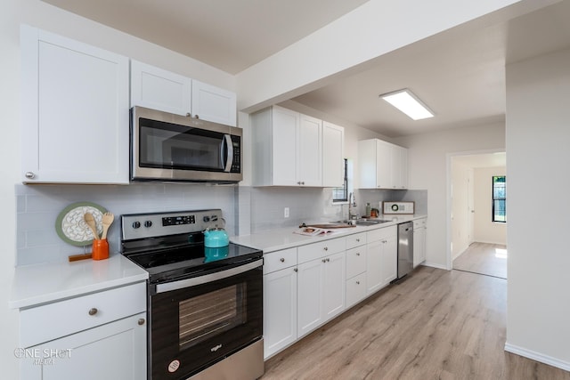 kitchen with light countertops, light wood-style flooring, decorative backsplash, appliances with stainless steel finishes, and white cabinetry