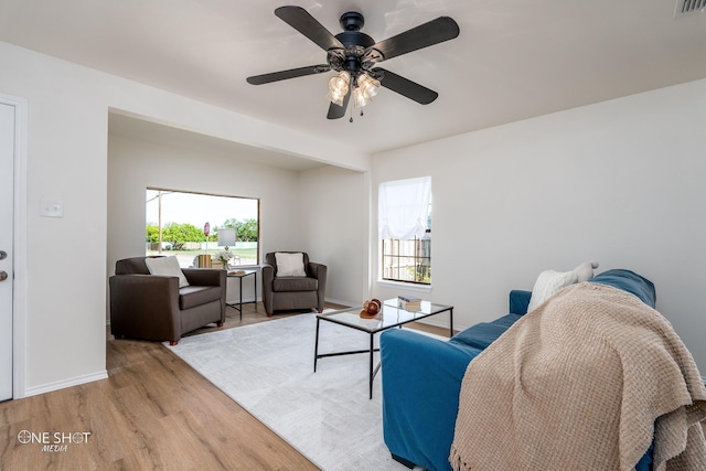 living area featuring a wealth of natural light, a ceiling fan, baseboards, and wood finished floors