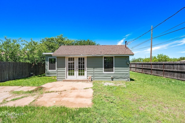 back of house with a fenced backyard, a shingled roof, an outdoor structure, french doors, and a lawn