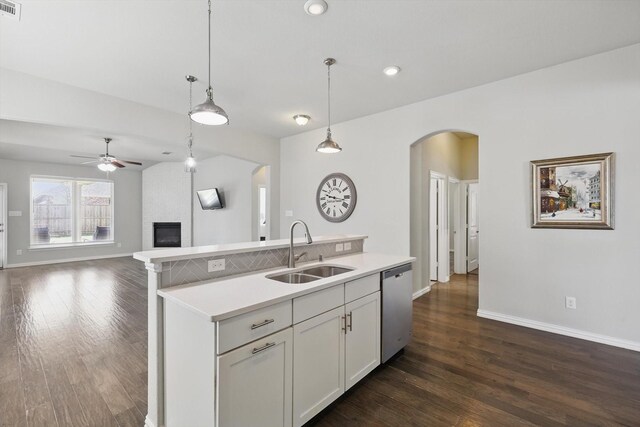 kitchen featuring dishwasher, a fireplace, arched walkways, a ceiling fan, and a sink