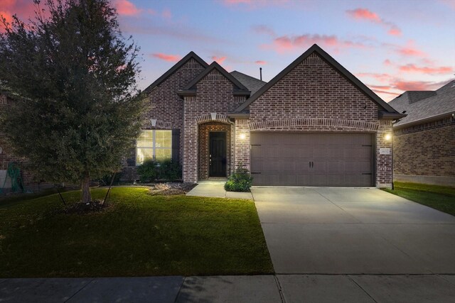 french country home featuring a front yard, driveway, a garage, and brick siding