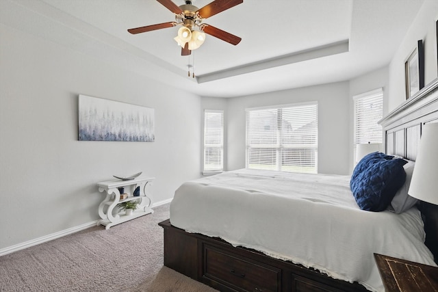 bedroom with baseboards, carpet, a tray ceiling, and a ceiling fan