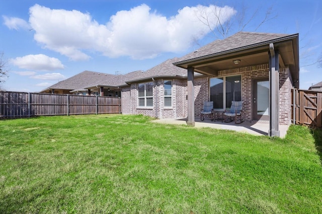 rear view of house featuring a patio area, a yard, a fenced backyard, and brick siding