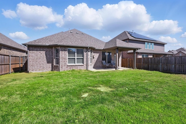 back of property with brick siding, a lawn, a fenced backyard, and roof with shingles