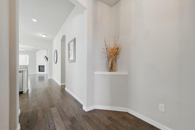 hallway featuring baseboards, arched walkways, and dark wood-type flooring