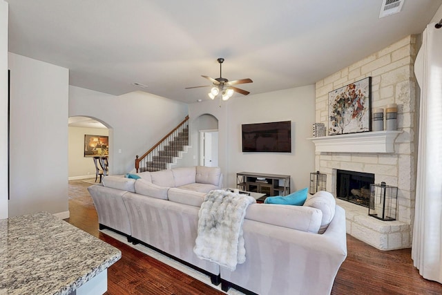 living room with arched walkways, a stone fireplace, dark wood-style floors, and visible vents