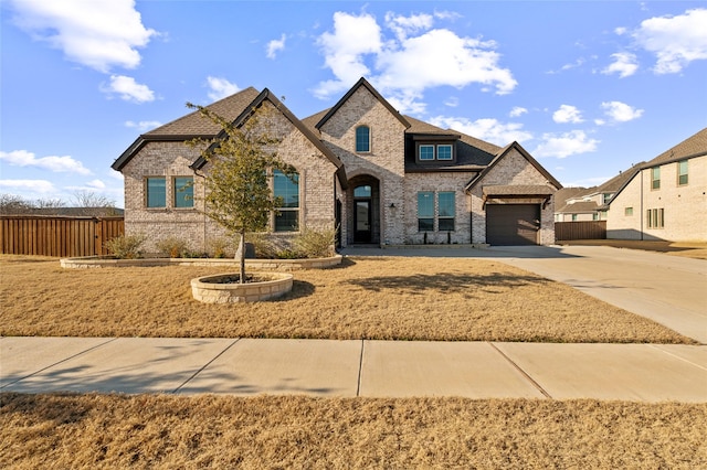 french country inspired facade featuring a garage, fence, brick siding, and driveway