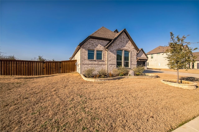 view of front of property featuring a shingled roof, fence, and brick siding