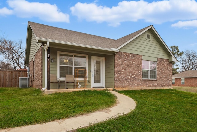 view of front of house featuring roof with shingles, brick siding, central air condition unit, fence, and a front lawn