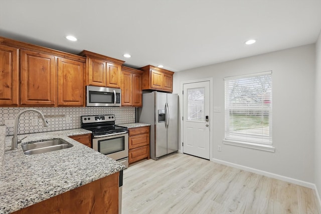 kitchen with light wood-style flooring, brown cabinets, a sink, stainless steel appliances, and backsplash