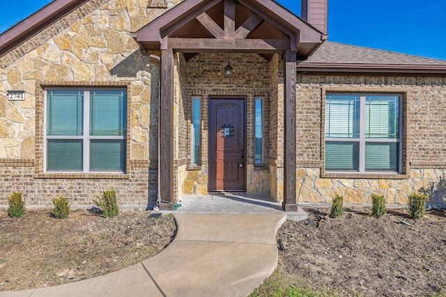 doorway to property featuring stone siding, brick siding, a chimney, and roof with shingles