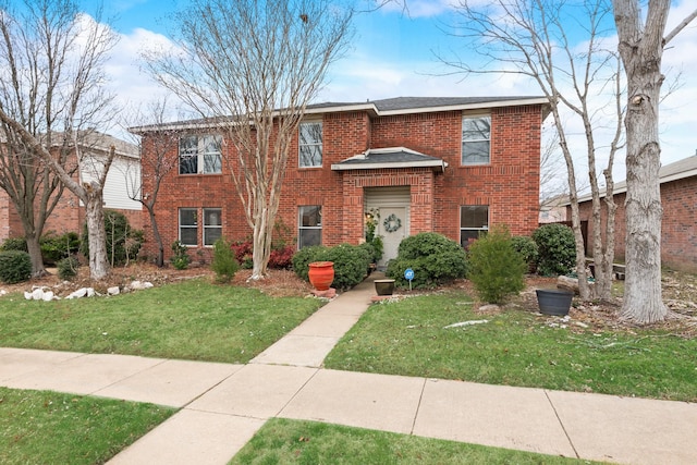 view of front facade with a shingled roof, a front yard, and brick siding