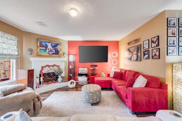 living room featuring visible vents, a brick fireplace, a textured ceiling, and wood finished floors