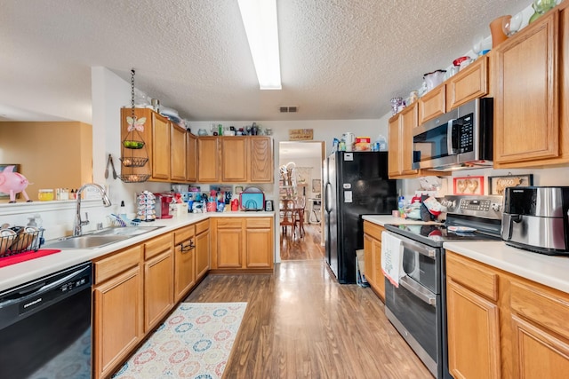 kitchen featuring a sink, visible vents, light countertops, light wood-type flooring, and black appliances