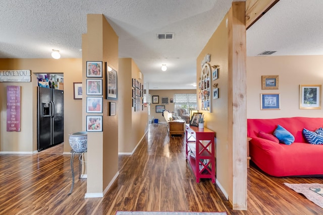 corridor with a textured ceiling, visible vents, and wood finished floors