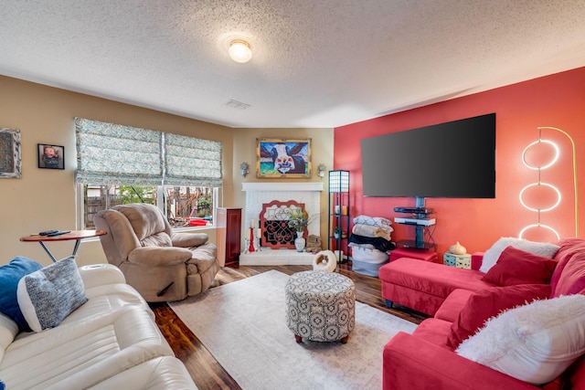 living room featuring a brick fireplace, visible vents, a textured ceiling, and wood finished floors