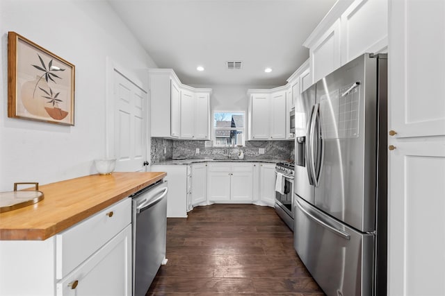kitchen with stainless steel appliances, butcher block countertops, visible vents, white cabinetry, and backsplash