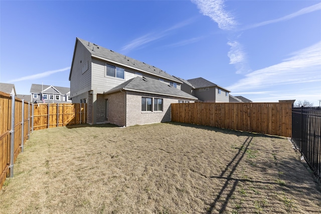 rear view of house featuring brick siding, a lawn, and a fenced backyard