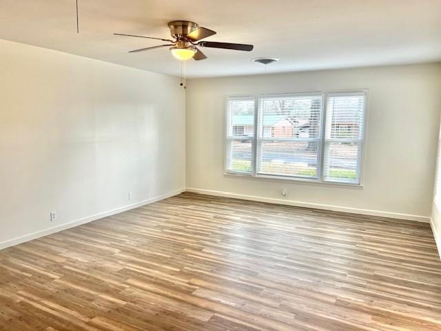 empty room with wood finished floors, a ceiling fan, and baseboards