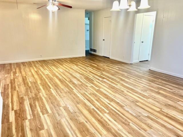 spare room with ceiling fan with notable chandelier, light wood finished floors, visible vents, and baseboards