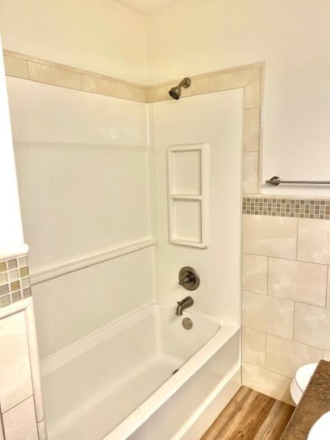 bathroom with shower / bath combination, tile walls, toilet, and wood finished floors