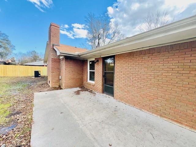 back of property featuring brick siding, fence, a chimney, and a patio