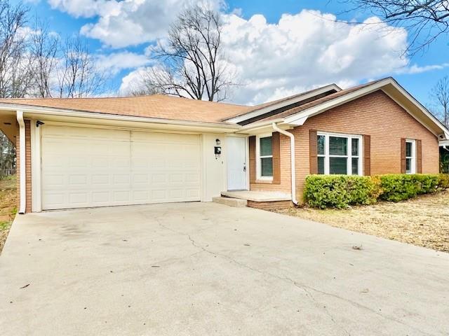 ranch-style home featuring an attached garage, concrete driveway, and brick siding