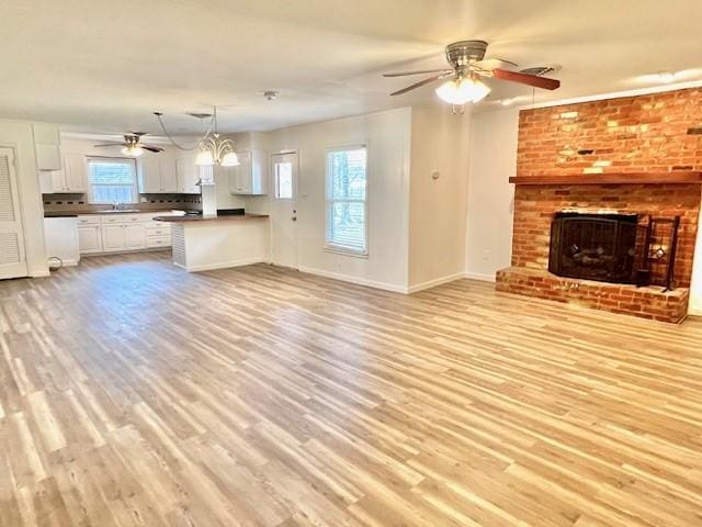 unfurnished living room with a fireplace, plenty of natural light, light wood-style flooring, and ceiling fan