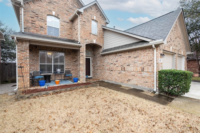 view of front of house featuring a shingled roof, a patio area, brick siding, and an attached garage