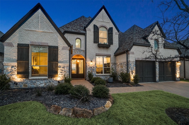 french country home featuring brick siding, a shingled roof, french doors, decorative driveway, and a garage