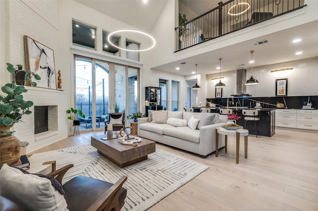 living room with visible vents, a high ceiling, a fireplace, and light wood finished floors