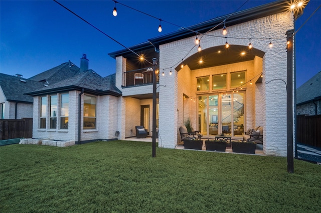 rear view of house featuring a lawn, a balcony, fence, brick siding, and a patio area